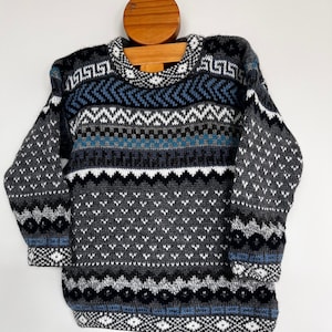 K&ouml;nnte beinhalten: Ein grauer, blauer und wei&szlig;er Pullover mit geometrischem Muster. Der Pullover hat ein geometrisches Muster mit einem sich wiederholenden Muster aus Dreiecken und Rauten.