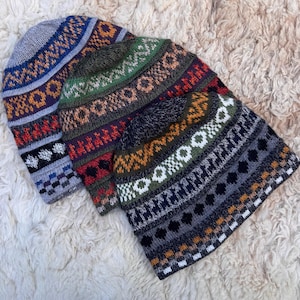 May include: Three knitted beanies with intricate geometric patterns in various colors. The hats feature designs in shades of blue, red, green, orange, and white. The beanies are displayed on a white, textured surface.
