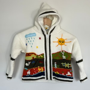 May include: White knitted zip-up hooded sweater with colourful embroidered details, including a sun, a cloud with raindrops, a house, and other nature-inspired elements.