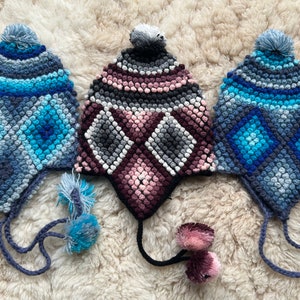 May include: Three crocheted hats with pom-poms. The hats are blue, pink, and gray with a diamond pattern. The hats have long ties.