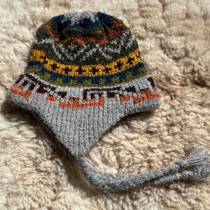 May include: A gray knitted hat with a colorful geometric pattern and a long tassel. The hat has a pointed crown and a wide brim.