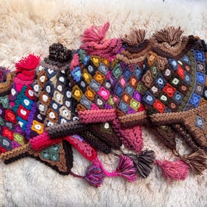 May include: A selection of colourful, hand-crocheted winter hats. Each hat features a unique diamond pattern in various colours, including red, blue, yellow, and green. The hats have ear flaps with tassels and a pom-pom on top, ideal for cold weather.