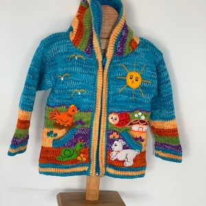 May include: A blue knitted hooded jacket with a zipper closure. The jacket features colorful stripes and embroidered animal designs, including a sun, a ladybug, a snail, a chicken, and a lamb.