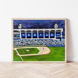 Puede incluir: Pintura acrílica de un estadio de béisbol por la noche. La palabra "RAYS" se muestra en la fachada del estadio. El campo es verde y el cielo es azul oscuro con estrellas y una luna creciente. La pintura está enmarcada.