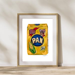 May include: A framed print of a yellow PAN cornmeal bag. The bag features a blue oval with the brand name "PAN", a corn illustration, and text indicating it contains 5 lbs of cornmeal. A woman with a red bow is also featured.