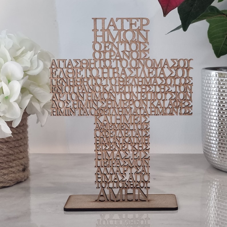Pode incluir: Uma cruz de madeira com a ora&ccedil;&atilde;o do Senhor em grego escrita nela. As palavras s&atilde;o cortadas na madeira, criando uma pe&ccedil;a &uacute;nica e decorativa.