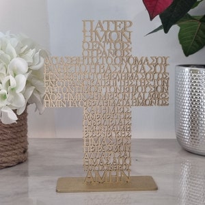 Pode incluir: Uma cruz de metal dourada com a ora&ccedil;&atilde;o do Pai Nosso em texto grego. A cruz est&aacute; sobre um suporte de metal dourado.