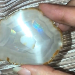 May include: A white agate slice with a brown edge and iridescent rainbow colors in the center.