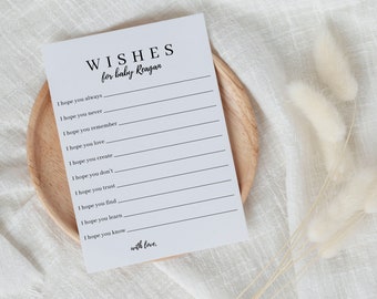 Pode incluir: Um cartão branco com texto preto que diz "WISHES for baby Reagar". O cartão tem uma lista de prompts que começam com "Espero que você sempre...", "Espero que você nunca...", e assim por diante.