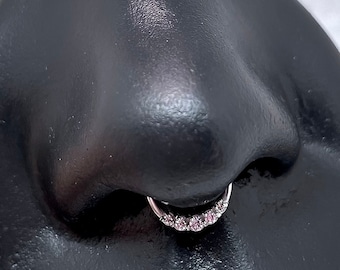 May include: A black nose ring display with a silver nose ring with small clear stones.