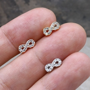 May include: Two infinity symbol earrings with clear cubic zirconia stones. One earring is gold and the other is silver.