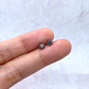 Pode incluir: Duas pe&ccedil;as de joalheria corporal prateadas com pequenas pedras preciosas redondas. A pe&ccedil;a &agrave; esquerda tem uma pedra preciosa branca iridescente, e a pe&ccedil;a &agrave; direita tem uma pedra preciosa azul escura.