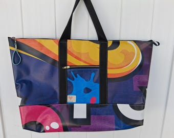 Può includere: Borsa tote di grandi dimensioni con un colorato design astratto. La borsa presenta una tasca con cerniera, manici neri e un tirazip blu. Il design include forme blu, gialle, arancioni, rosa e viola. La borsa è realizzata in materiale resistente.