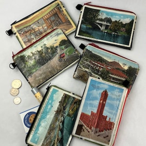 May include: Six small zippered pouches made from vintage postcards. Each pouch features a different image of a city scene, including a bridge, a building, and a street.
