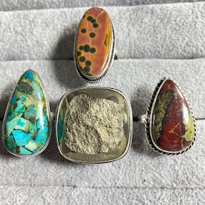 May include: Four silver rings with different gemstone settings. The rings feature a variety of colors and patterns, including turquoise, red, green, and gold.