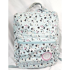 May include: A light blue backpack with a floral pattern of black, white, and pink flowers. The backpack has a top handle, a front zippered pocket, and adjustable shoulder straps. A pink and white logo is on the front.