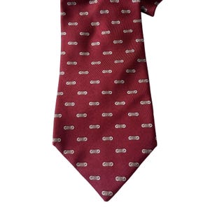 May include: Burgundy-colored tie with a repeating pattern of the letters "GHID" in white. The tie is made of a smooth fabric and is suitable for formal or business attire.