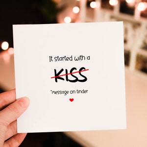 May include: A white card with the text "It started with a kiss" with a red line through the word "kiss" and the text "message on tinder" below. A small red heart is at the bottom of the card.