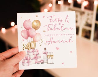 Op de afbeelding: Roze verjaardagskaart met de tekst "Forty & Fabulous" en "Happy 40th Birthday Hannah". De kaart bevat illustraties van ballonnen, cadeaus, champagne en glazen.