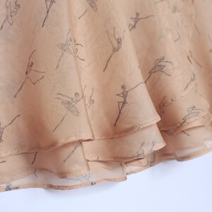 Pu&ograve; includere: Una gonna rosa pallido con una delicata stampa di ballerine. La gonna ha un design a balze sovrapposte sul bordo.