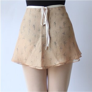 Pu&ograve; includere: Una gonna da ballet beige a doppio strato con un nastro bianco da legare. La gonna &egrave; stampata con un motivo di ballerini in grigio chiaro.