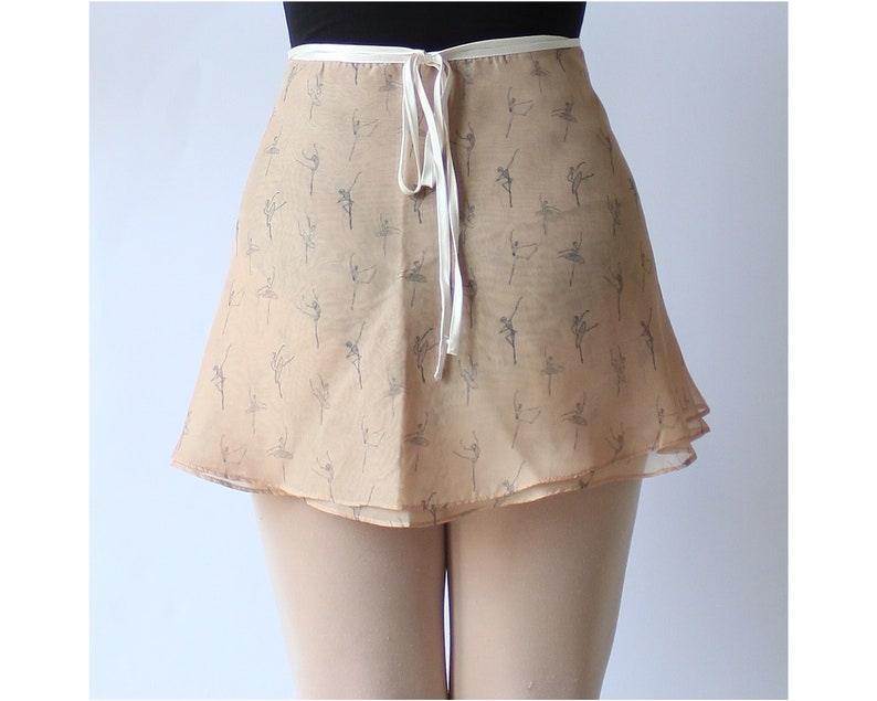 Pu&ograve; includere: Una gonna da ballet beige a doppio strato con un nastro bianco da legare. La gonna &egrave; stampata con un motivo di ballerini in grigio chiaro.