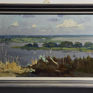 May include: Oil painting of a landscape with a river, trees, and a cloudy sky. The artwork is framed in a gray wooden frame. The painting depicts a serene natural scene with muted colors.