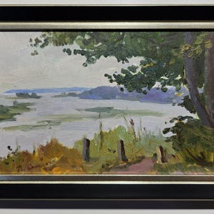 May include: Oil painting of a landscape scene with a lake and trees. The artwork is framed in a black and gold frame. The painting features a path, water, and foliage in shades of green, blue, and yellow.