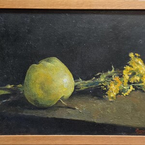 May include: Oil painting of a still life featuring a green apple and yellow flowers against a dark background. The artwork is framed in a light-colored wooden frame, showcasing the natural tones of the subject matter.