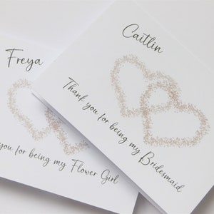 May include: Two white cards with black text and a brown heart design. The top card says "Caitlin Thank you for being my Bridesmaid". The bottom card says "Freya Thank you for being my Flower Girl".