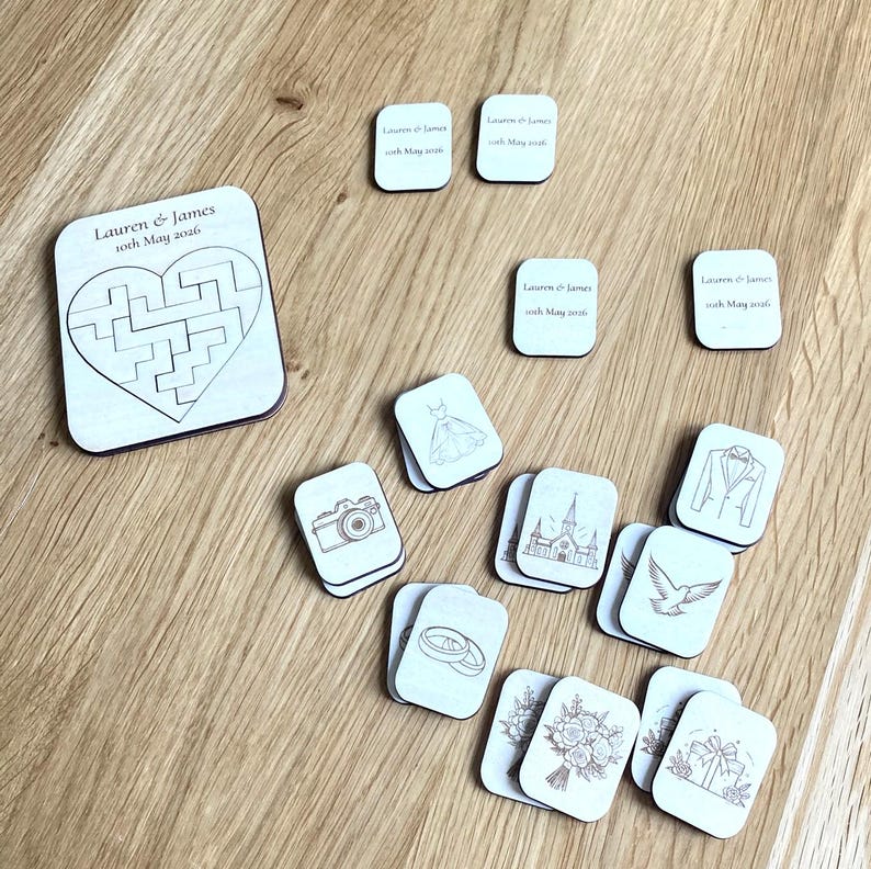 K&ouml;nnte beinhalten: Ein Set aus hellen Holz-Puzzleteilen und rechteckigen Pl&auml;ttchen mit Hochzeitsmotiven. Das gr&ouml;&szlig;te Teil zeigt ein herzf&ouml;rmiges Labyrinth und den Text Lauren & James 10th May 2026. Kleinere Pl&auml;ttchen zeigen eingravierte Symbole wie Kamera, Kleid, Kirche, Ringe, Taube, Blumenstrau&szlig; und Geschenk.