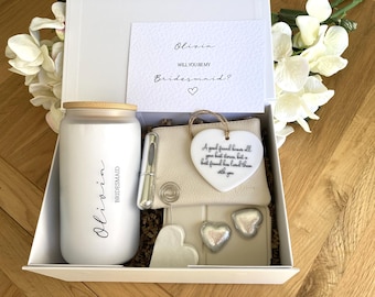 Könnte beinhalten: Eine weiße Geschenkbox mit einem mattierten Glasbecher mit Bambusdeckel, beschriftet mit Olivia Bridesmaid, einem beigen Reißverschlusstäschchen, einem herzförmigen Keramikornament mit Text, einem silbernen Stift und zwei kleinen silbernen Herzen.