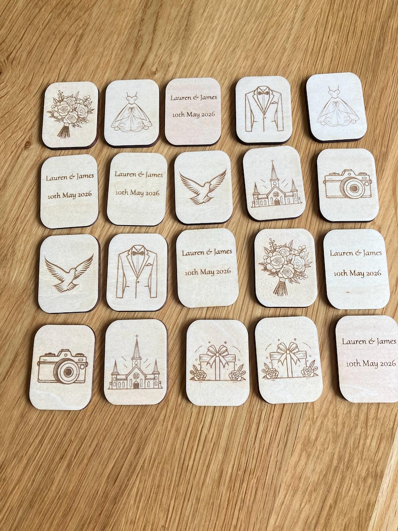 K&ouml;nnte beinhalten: Eine Sammlung rechteckiger Holzpl&auml;ttchen mit lasergravierten Hochzeitsmotiven wie Blumenstr&auml;u&szlig;en, Kleidern, Anz&uuml;gen, Kirchen, Kameras, Tauben und Geschenken sowie dem Text Lauren & James 10th May 2026.
