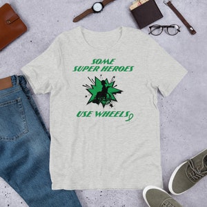 May include: A heather grey t-shirt with a green graphic of a person in a wheelchair with the text "Some Super Heroes Use Wheels" and a green ribbon.