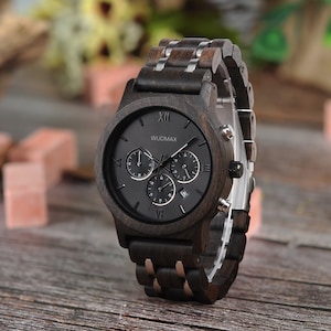 Könnte beinhalten: Eine schwarz-braune Armbanduhr aus Holz mit einem Chronographen-Zifferblatt. Das Zifferblatt der Uhr hat römische Ziffern als Stundenmarkierungen und den Markennamen "WUDMAX" aufgedruckt.