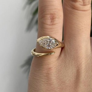 Puede incluir: Un anillo de oro tipo bypass con una piedra preciosa transparente en forma de pera montada en una banda de oro pulido. El diseño abierto permite que los extremos de la banda se superpongan ligeramente, con la piedra facetada en un extremo.