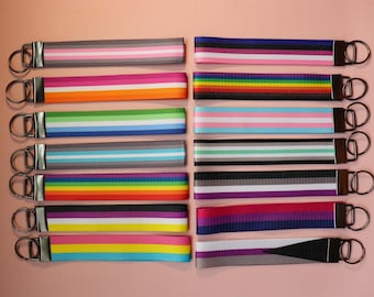 May include: A collection of keychains with various striped patterns in colors like pink, orange, green, blue, and rainbow. Each keychain has a metal ring and a brown leather-like loop.