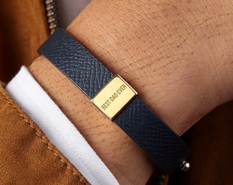 Puede incluir: Un brazalete de cuero azul marino con una placa dorada que dice "Best Dad Ever".