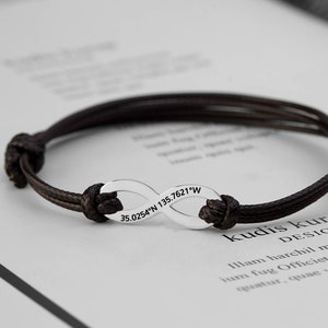 May include: A brown cord bracelet with an infinity charm engraved with the coordinates "35.0254°N 135.7621°W" and the text "kudis kurap DESIGNER".