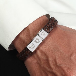 May include: Brown leather bracelet with a silver charm engraved with "MAEVE 1.29.21" and a footprint symbol. The other charm is engraved with "7 LBS 4 OZ".