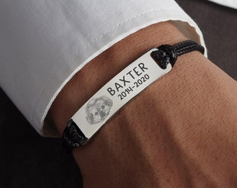 Puede incluir: Un brazalete de cuero negro con una etiqueta rectangular de plata grabada con el nombre "BAXTER" y las fechas "2014-2020". Una pequeña cara de perro está grabada en la etiqueta.