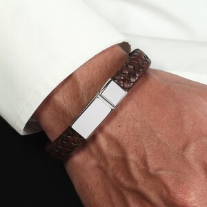 May include: A brown leather braided bracelet with a silver rectangular plate.