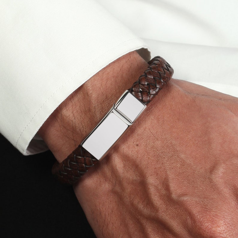 May include: A brown leather braided bracelet with a silver rectangular plate.