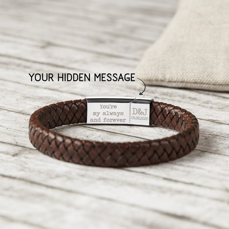 May include: Brown leather bracelet with a silver clasp. The clasp has an engraved message that reads "You're my always and forever D&J 05.28.2020".