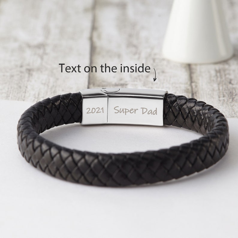 May include: Black leather braided bracelet with a silver clasp. The clasp is engraved with the text "2021 Super Dad".