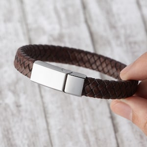 May include: A brown leather bracelet with a silver clasp. The bracelet is woven in a braided pattern.
