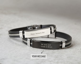 Op de afbeelding: Twee zwarte siliconen armbanden met zilveren accenten en gegraveerde metalen platen. De bovenste armband heeft de tekst "Happy Father's Day" gegraveerd op de plaat. De onderste armband heeft de tekst "We love you! - Linda & Brian" gegraveerd op de plaat.