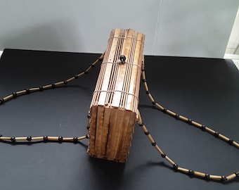 May include: A rectangular bamboo purse with a black beaded strap. The purse is made of woven bamboo strips and has a simple design.