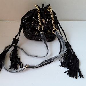 May include: A black sequined bucket bag with a gold chain strap and tassel accents. The bag has a drawstring closure and a long adjustable strap.