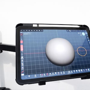May include: A black tablet with a protective case displays a 3D modeling program, showcasing a white sphere on a grid. A stylus rests on the tablet's edge. The tablet is mounted on a black adjustable arm, set against a white background.
